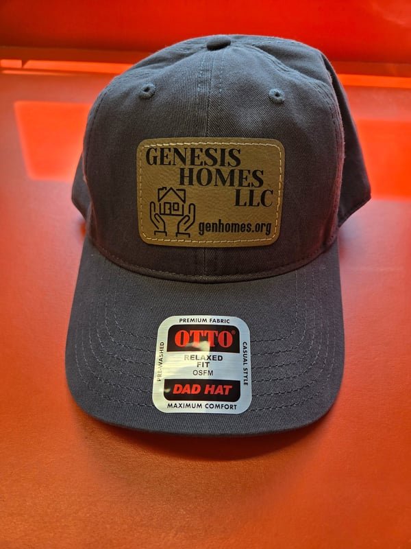 A grey cap with a leather patch engraved with the Genesis Homes LLC logo.