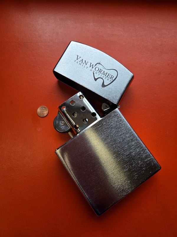 An open brushed steel lighter fiber-engraved with the Van Wormer Family Dentistry logo.