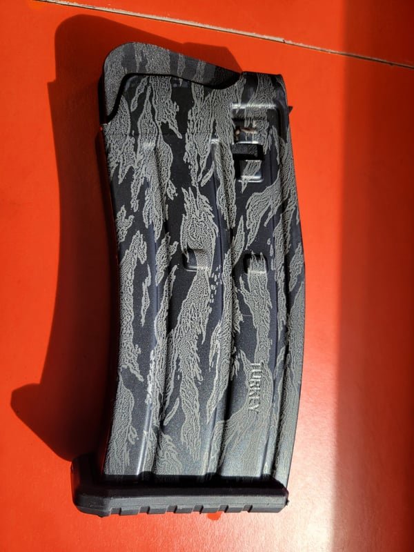 A rifle magazine in tiger-stripe camouflage, fiber-engraved along its body.