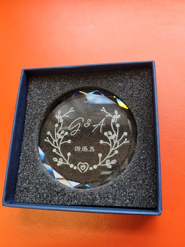 A round glass ornament in a gift box, engraved with the monogram G and A and the date 09.05.25.