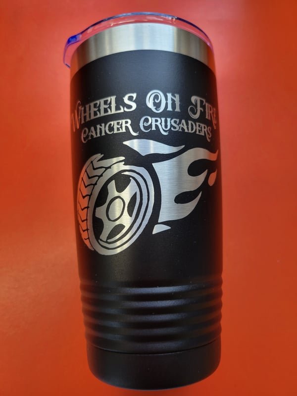 A black tumbler engraved with the Wheels On Fire Cancer Crusaders flaming-wheel logo.