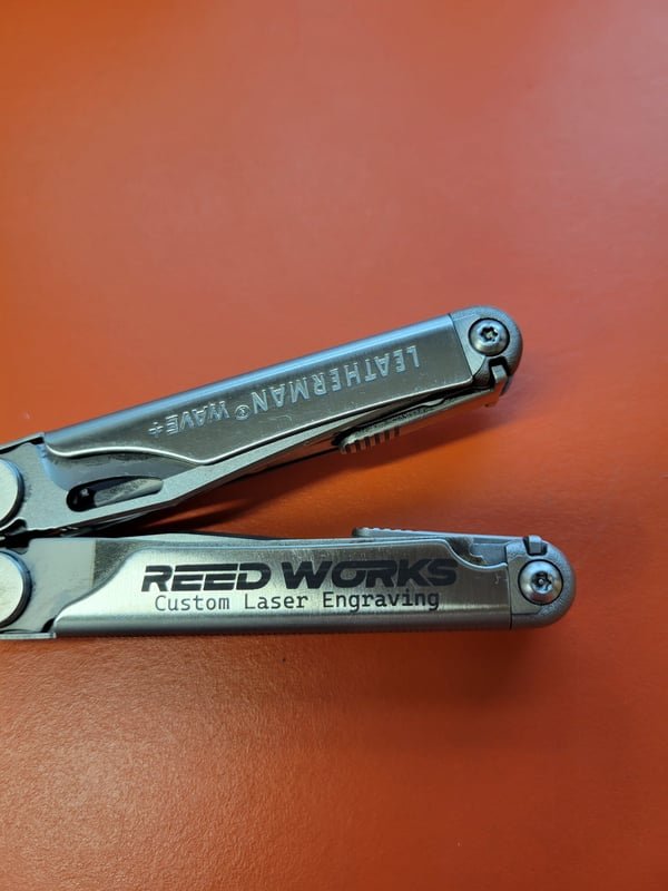 A Leatherman Wave multitool fiber-engraved with the Reed Works name along the handle.