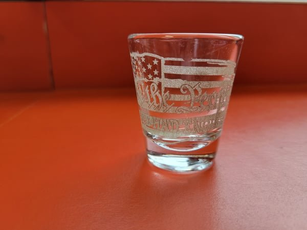 A shot glass etched with an eagle and flag motif.