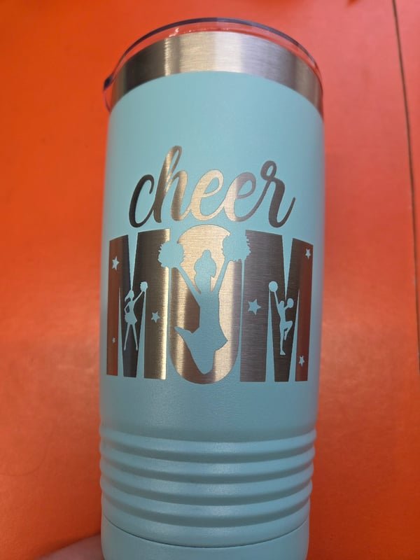 A pale blue tumbler engraved with cheerleader silhouettes and the words Cheer Mom.