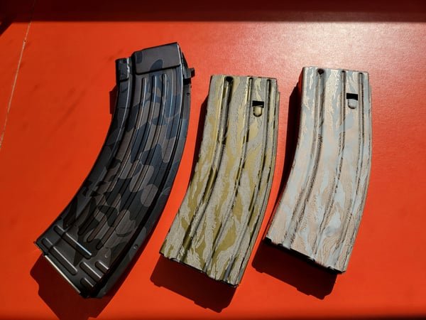 Three rifle magazines in different camouflage finishes, each fiber-engraved.