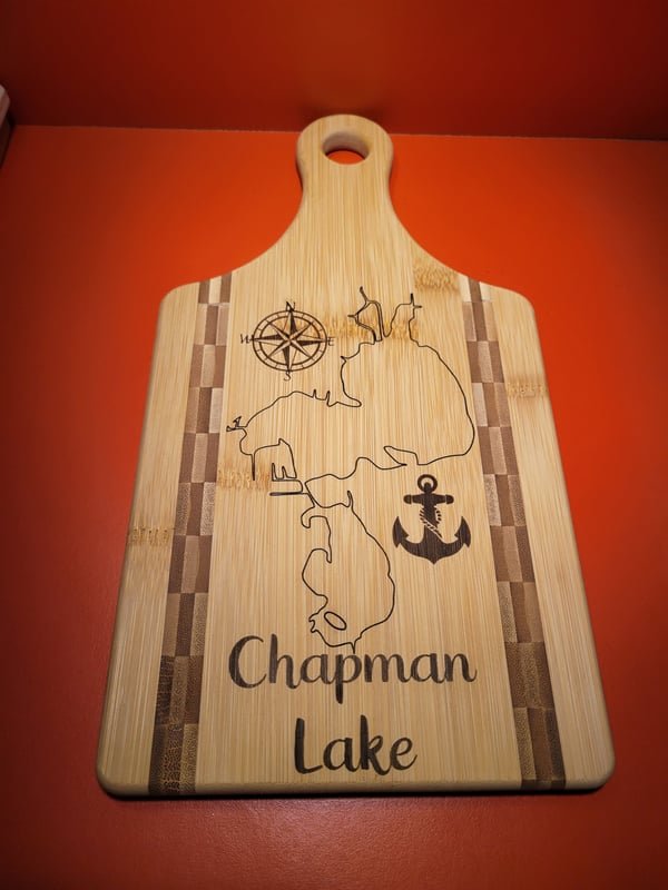 A bamboo paddle board engraved with a map of Chapman Lake, a compass rose and an anchor.