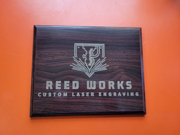 A dark plaque engraved with the Reed Works Custom Laser Engraving logo.