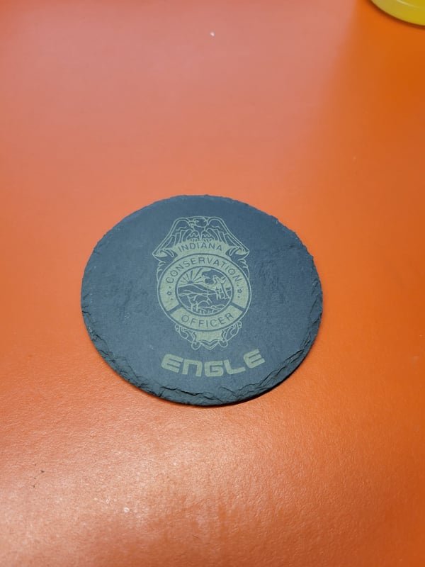 A round slate coaster engraved with the Indiana Conservation Officer badge and the name Engle.