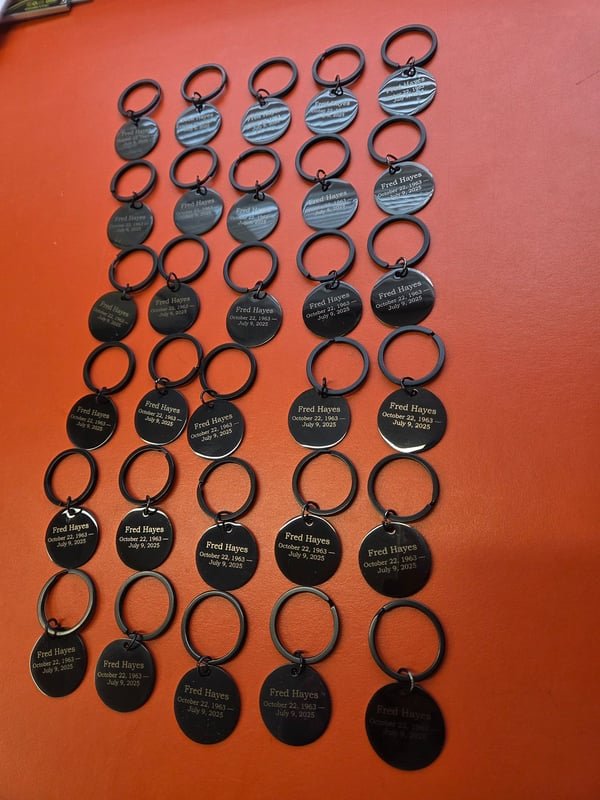 Dozens of memorial keyring tags on rings, each engraved with the same name and dates.