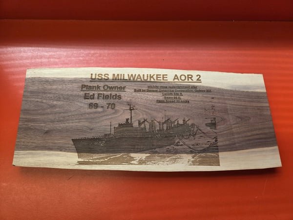 A live-edge wood plaque engraved with the USS Milwaukee AOR 2, its specifications and plank owner Ed Fields.