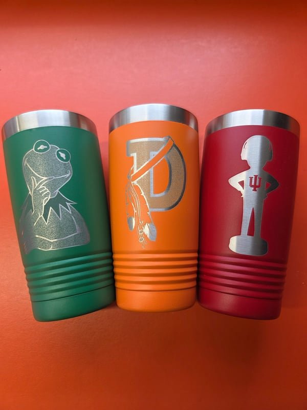 Three tumblers in green, orange and red, each engraved with a different team or character mascot.