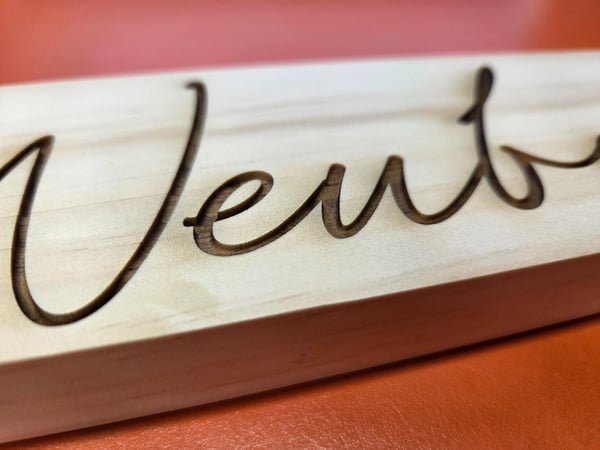 A pale wood sign engraved in deep flowing script with a family name.