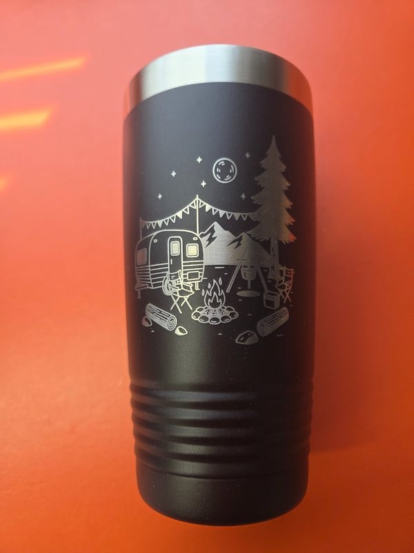 A black tumbler engraved with a camping scene of a caravan, campfire and pine trees under a moon.