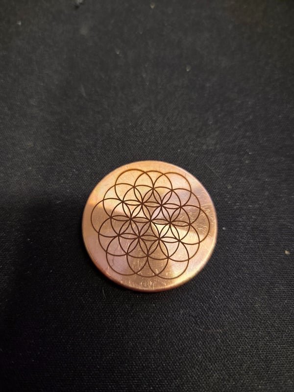 A copper disc fiber-engraved with a fine Flower of Life geometric pattern.