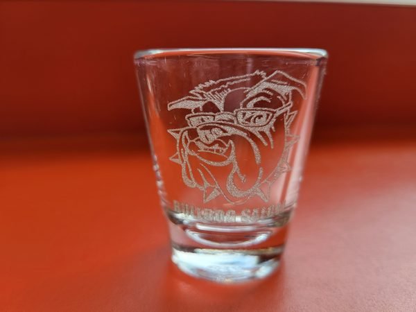A clear shot glass etched with a sunglasses-wearing bulldog above the words Bulldog Saloon.