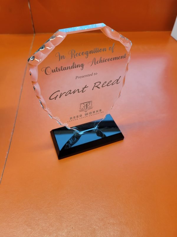 A faceted glass award on a black base, engraved In Recognition of Outstanding Achievement for Grant Reed.