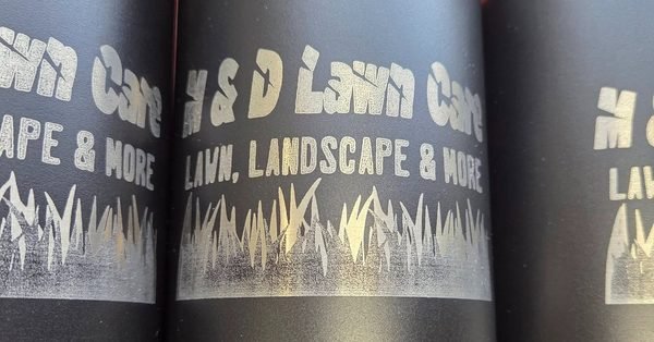 A close-up of black bottles engraved with the H&amp;D Lawn Care, Landscape and More logo above a grass silhouette.