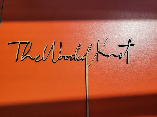 A black acrylic cake topper cut in long flowing script reading The Wooded Knot.