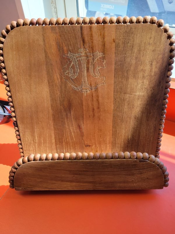 A wooden cookbook stand edged with beads, engraved with an interlocking monogram.