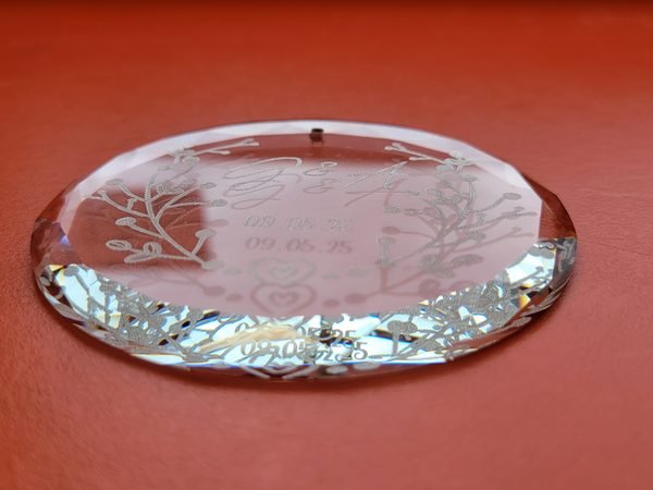 A close-up of a bevelled glass ornament, the engraved monogram and wedding date catching the light.