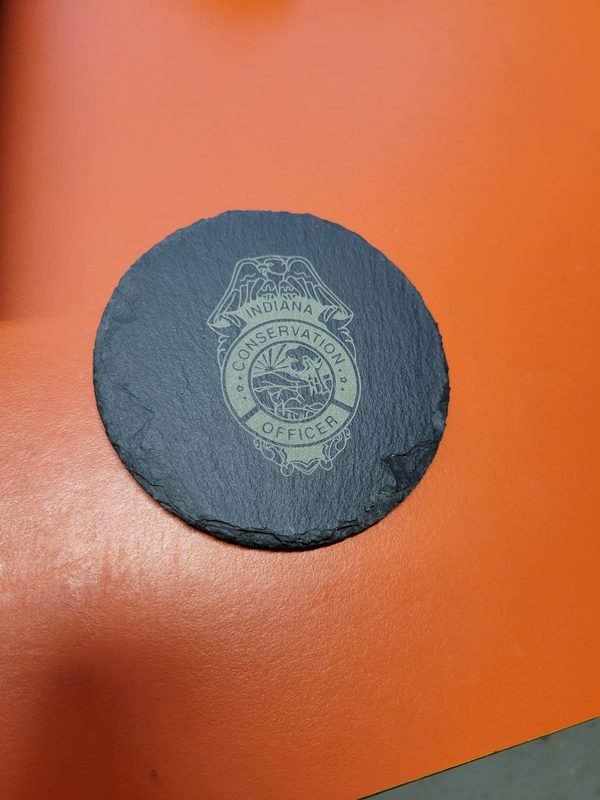 A round slate coaster engraved with the Indiana Conservation Officer badge.