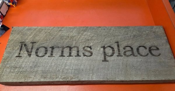 A weathered barn-wood sign engraved with the words Norms place.