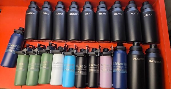 A boxed bulk order of insulated bottles in black and pastel colours, each engraved with a staff member's name.