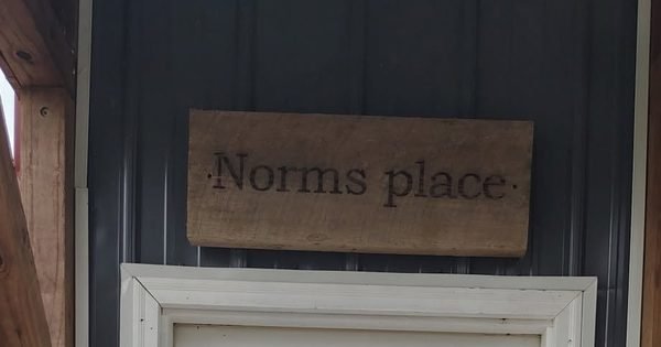 The Norms place barn-wood sign mounted above a doorway on a navy clapboard building.