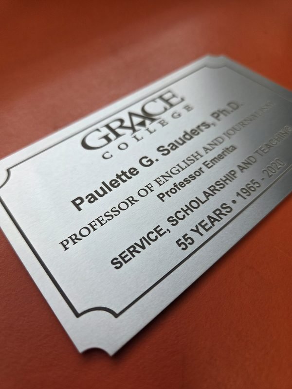 A close-up of a brushed metal Grace College plaque, the engraved lettering standing dark against the satin finish.