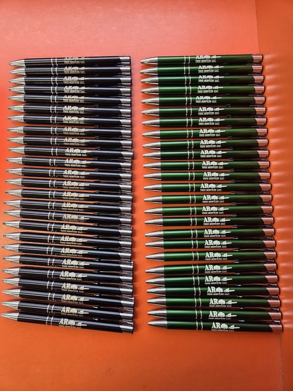 Black and green promotional pens laid out in two ranks, each engraved with a tree service logo.