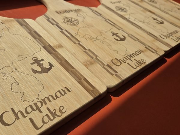 A close-up of a Chapman Lake paddle board, the anchor and script lettering cut deep into the bamboo.