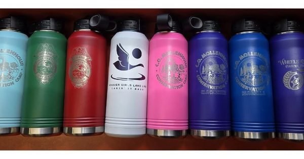 A row of insulated bottles in teal, green, red, white, pink and blue, each engraved with a different club crest.