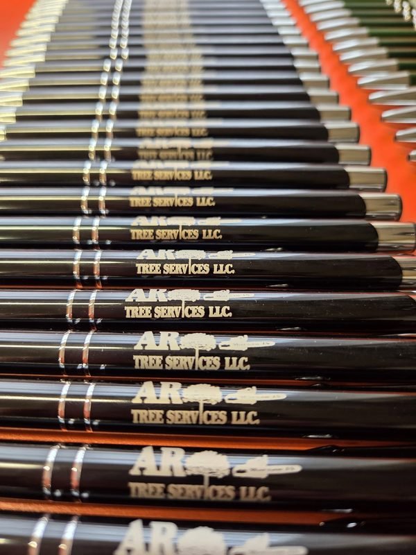 A close-up of black metal pens engraved with the AR Tree Services LLC name and tree mark.