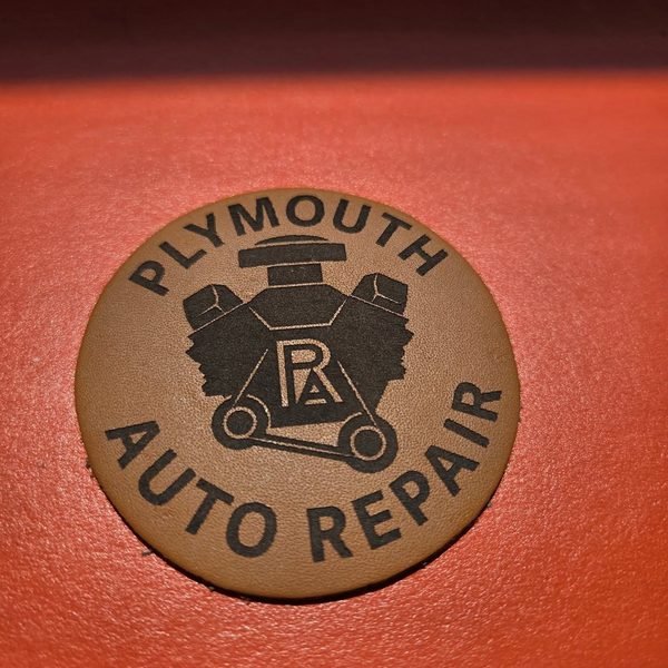 A round leather patch engraved with the Plymouth Auto Repair engine-block logo.