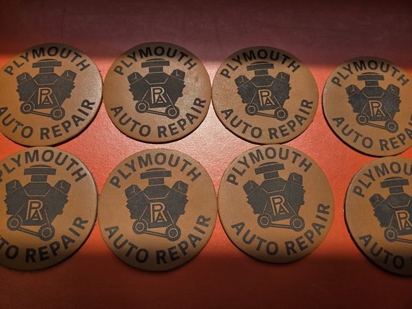 Round leather patches laid out in rows, each engraved with the Plymouth Auto Repair logo.