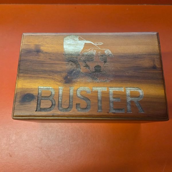 A cedar box engraved with a swimming dog and the name Buster in deep block letters.