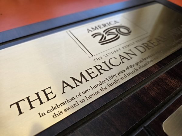 A close-up of the brushed gold plate on the America 250 American Dream Award, its dedication deeply engraved.