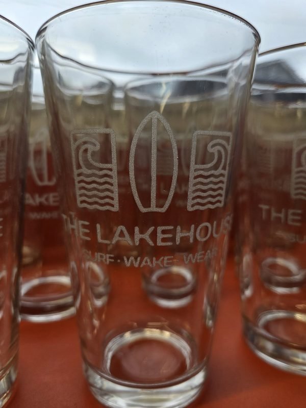 Pint glasses etched with a surfboard and wave logo reading The Lakehouse, Surf Wake Wear.