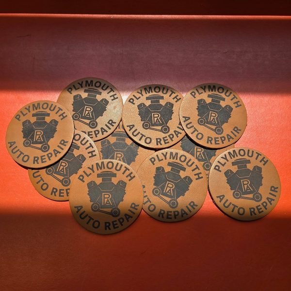 A loose pile of engraved Plymouth Auto Repair leather patches.