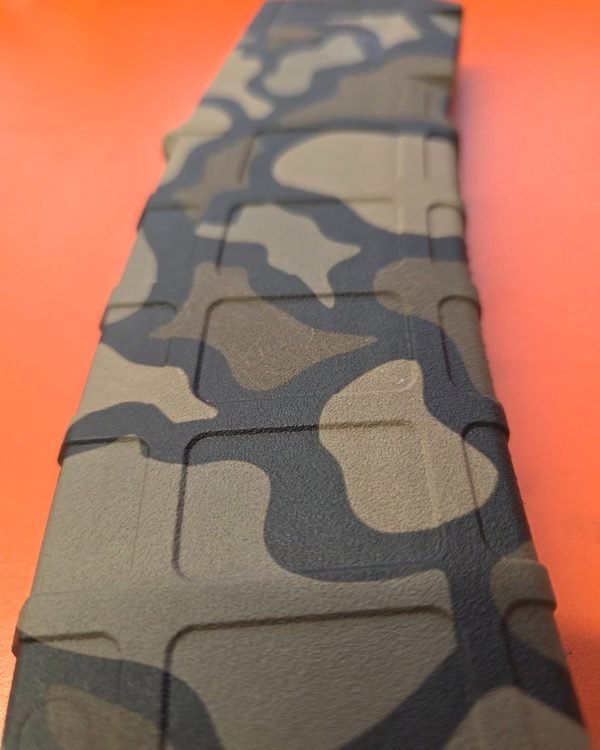 A close-up of a camouflage rifle magazine, the fiber-engraved pattern running along its body.