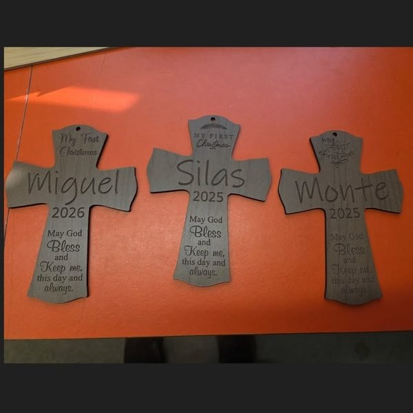 Three wooden crosses engraved with the names Miguel, Silas and Monte beneath a My First Christmas blessing.