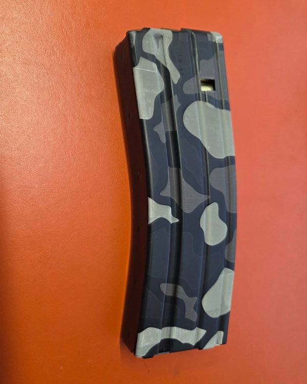 A rifle magazine in blue and grey camouflage, fiber-engraved along its curved body.