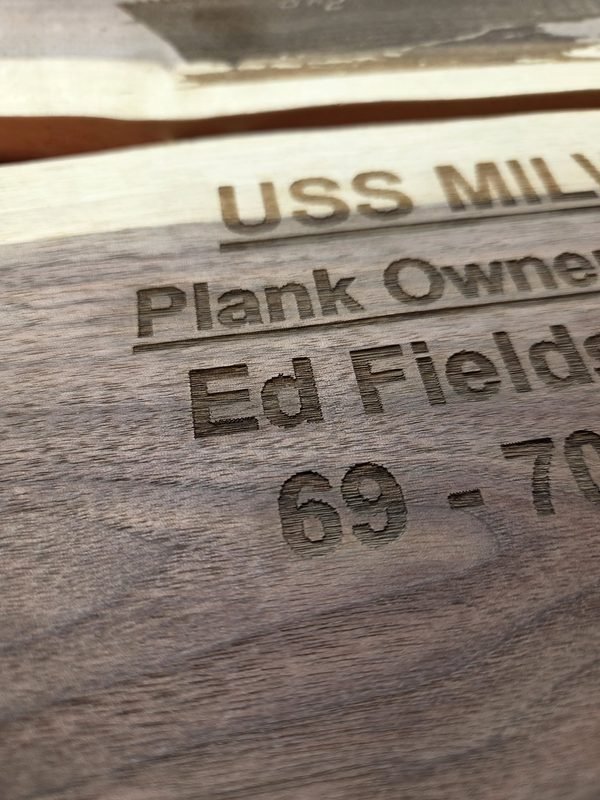 A close-up of a walnut plaque engraved USS Milwaukee, Plank Owner, Ed Fields, 69 to 70.