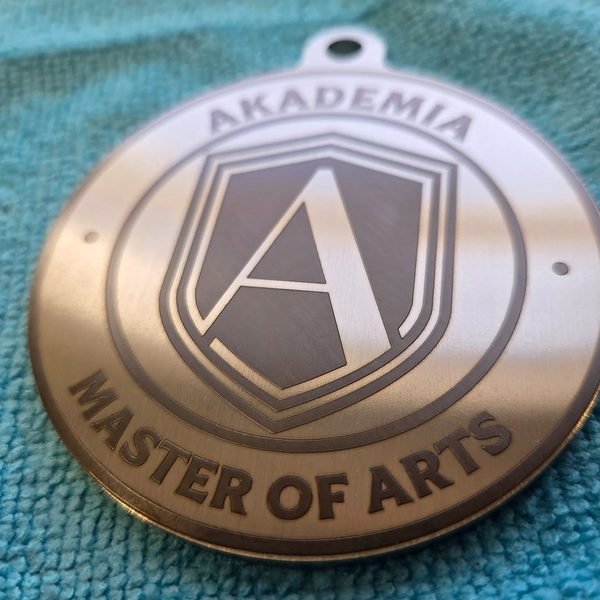 A steel medallion fiber-engraved with the Akademia Master of Arts shield.