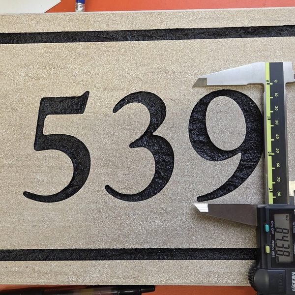Digital calipers measuring the depth of the numerals cut into a stone address sign.