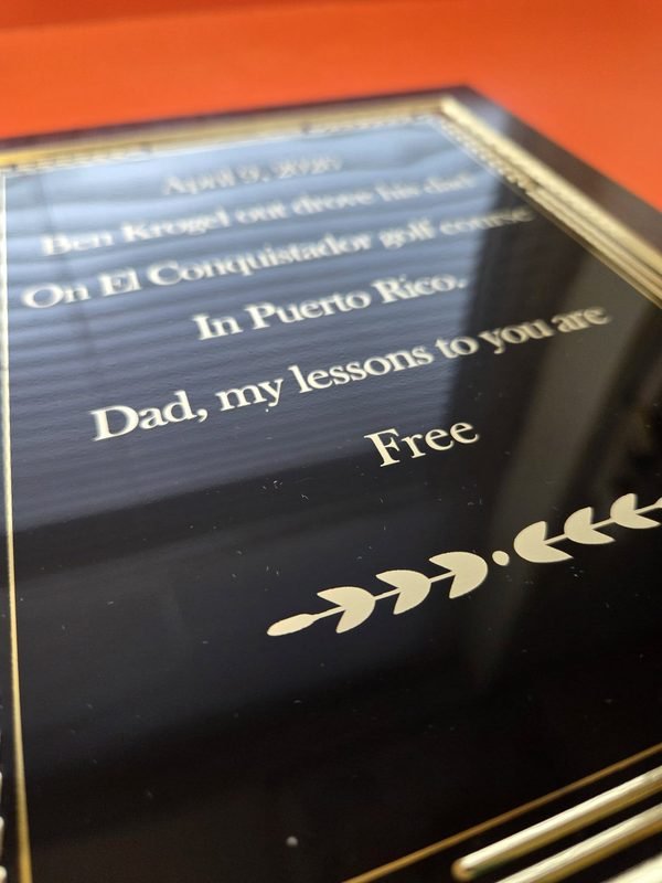 An angled view of a black and gold plaque engraved with a humorous tribute to a round of golf in Puerto Rico.