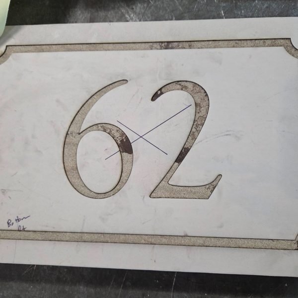 A stone address plaque on the laser bed, the numerals and border freshly cut into the face.