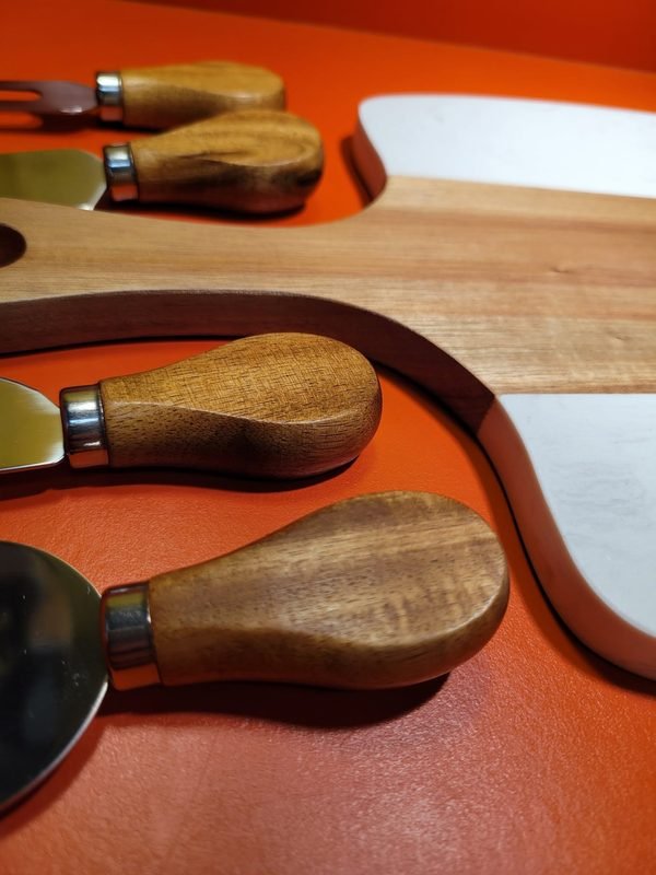 Cheese knives with turned wooden handles resting on a marble and wood serving board.