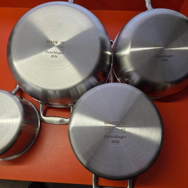 Three stainless pans arranged base-up, each fiber-engraved with the Oelschlager name and 2026.