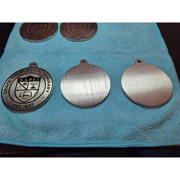 Engraved Grace Theological Seminary medallions beside blank steel discs on a polishing cloth.